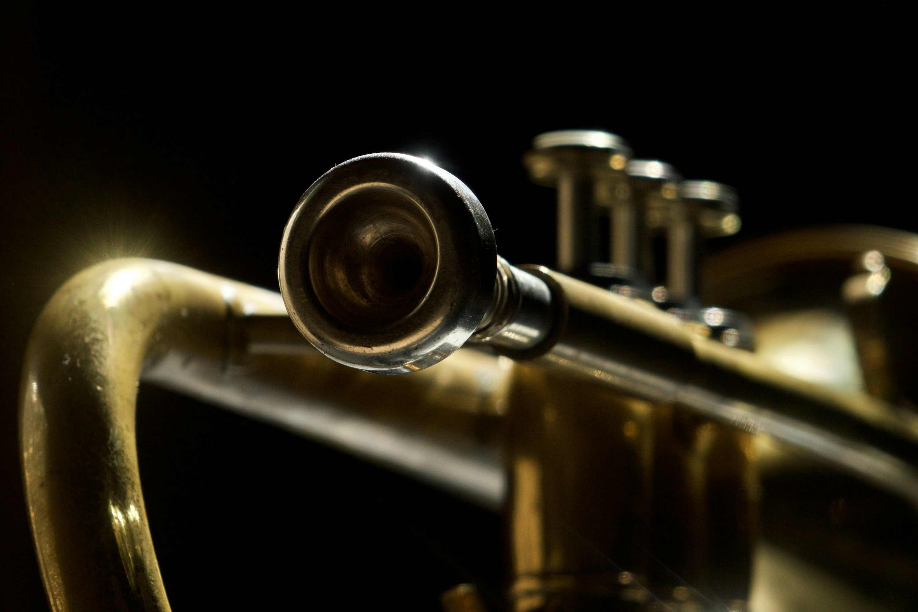A close-up photograph looking toward the mouthpiece of a worn brass trumpet against a dark background